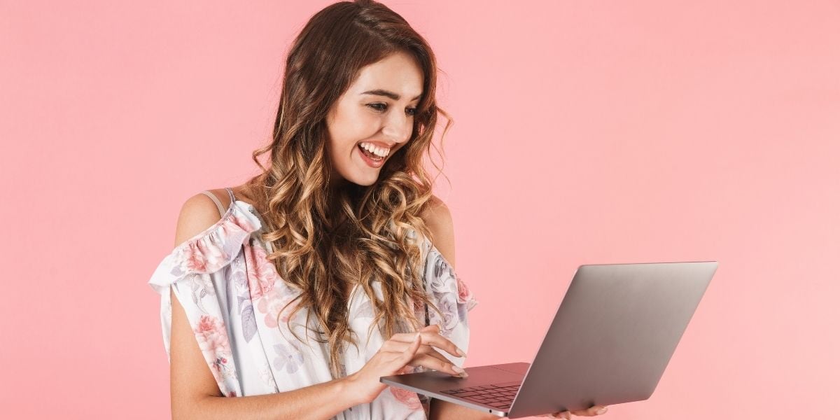 A woman smiling at her laptop showing a list of the best places to sell jewelry online